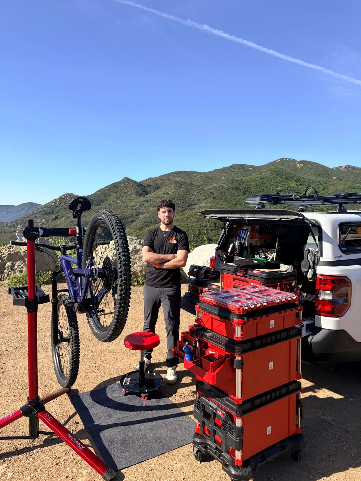 Shlomi with his full mobile workshop — repair stand, bike and stacked tool cases in the Los Angeles mountains